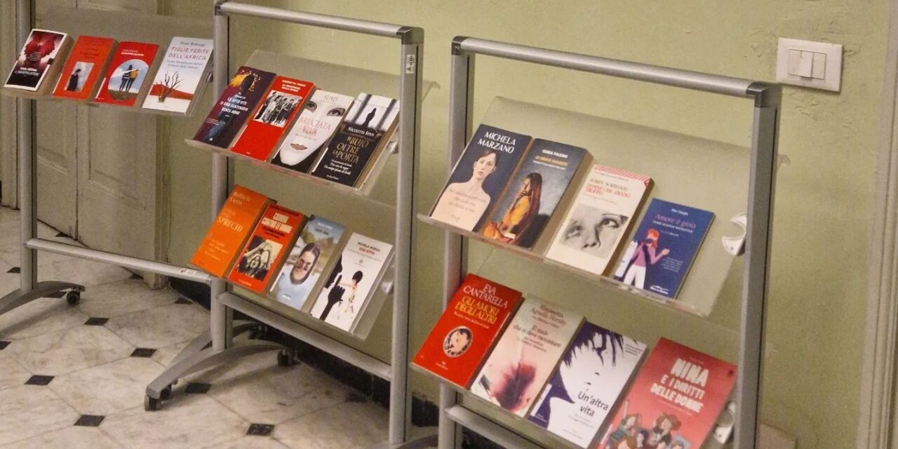 Uno scaffale di libri in Biblioteca a Tortona contro la violenza sulle donne per Giornata dedicata